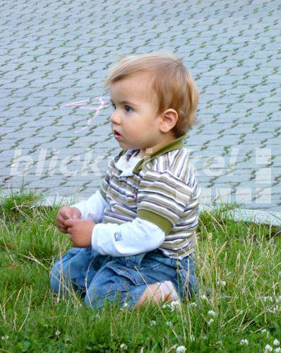 blickwinkel - kleiner Junge sitzt in einer Wiese, im Hintergrund