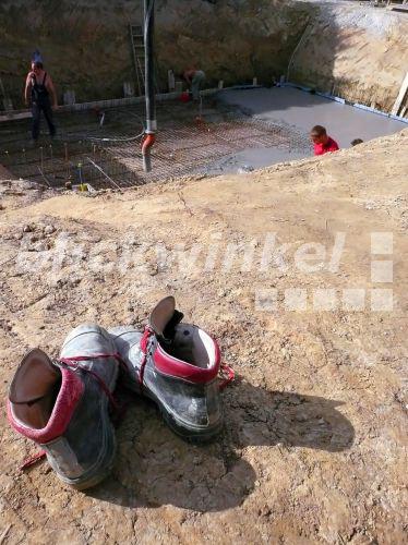 blickwinkel - Bauarbeiter giessen eine Betonbodenplatte fuer ein Haus, im Vordergrund ein paar ...